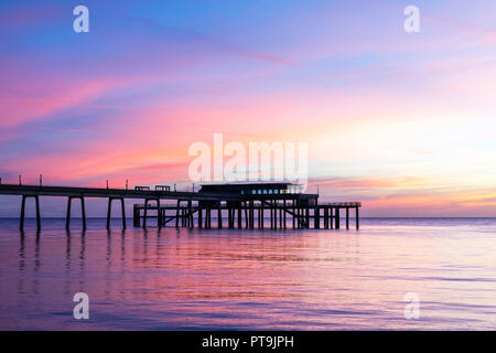 Trattare pier con un mare calmo e il sorgere del sole sul mare orizzonte in un cielo parzialmente chiara e in parte con soffice nuvola di sottili strati. Foto Stock