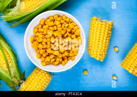 Mais maturo su una tabella blu close-up. Materie e conserve di mais in una ciotola bianca, vista dall'alto. Foto Stock