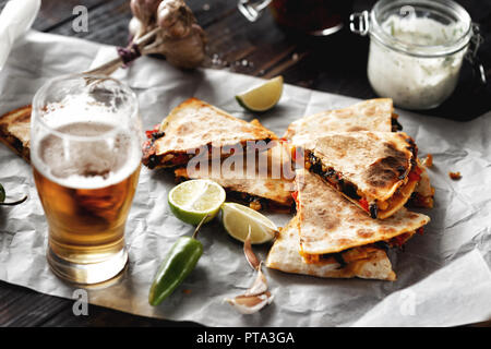 Birra vegetariano snack: quesadilla con verdure e formaggio in legno scuro con piano in vetro di birra lager Foto Stock