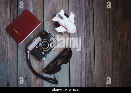 Un passaporto, vintage fotocamera, piccoli velivoli e occhiali da sole su sfondo di legno Foto Stock