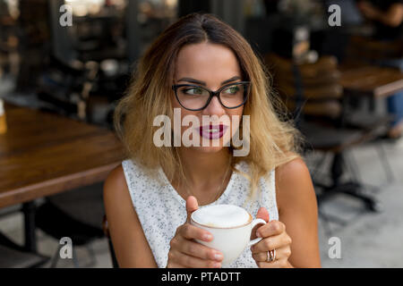 Portarit di un business donna che indossa gli occhiali in cornice nera e di bere il caffè di mattina in un bar. Foto Stock
