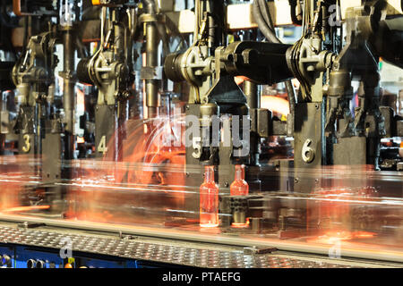 Hot bottiglie in vetro su una linea di produzione di vetro piano. Caldo rosso bottiglie avanzano lungo il trasportatore in fabbrica Foto Stock