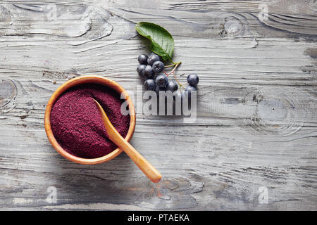 Aronia organici in polvere in un recipiente con fresche bacche di Aronia sul tavolo. Foto Stock