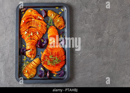 Tagliate a fettine sottili tutta la zucca cotta in forno con cipolla rossa di timo fresco e spezie su un vassoio da forno su un sfondo di calcestruzzo, vista da sopra, piana, laici copia s Foto Stock