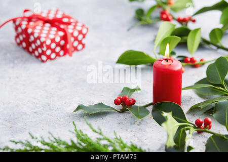 Le decorazioni di Natale, candela con decorazioni di sempreverdi. Foglie di agrifoglio con bacche rosse. Foto Stock