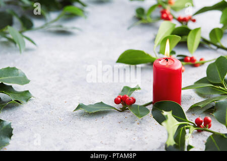 Le decorazioni di Natale, candela con decorazioni di sempreverdi. Foglie di agrifoglio con bacche rosse. Foto Stock