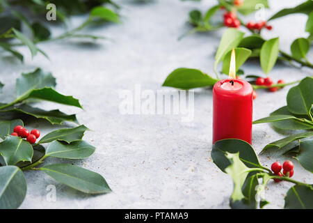 Le decorazioni di Natale, candela con decorazioni di sempreverdi. Foglie di agrifoglio con bacche rosse. Foto Stock