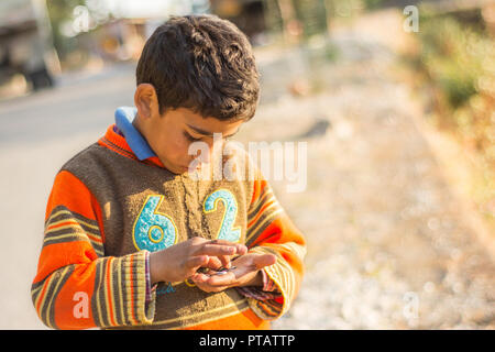 La foto di un ragazzo indiano guardando verso il basso e contare monete nelle sue mani nel pomeriggio a Mussourie, Uttarakhand Foto Stock