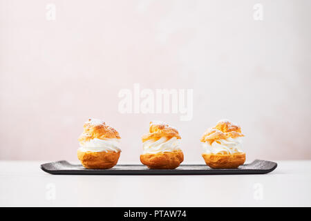 Deliziosa crema torte di sfoglia con panna e zucchero a velo su una piastra di nero su bianco tavola di marmo su sfondo rosa. Messa a fuoco selettiva, copia dello spazio. Foto Stock