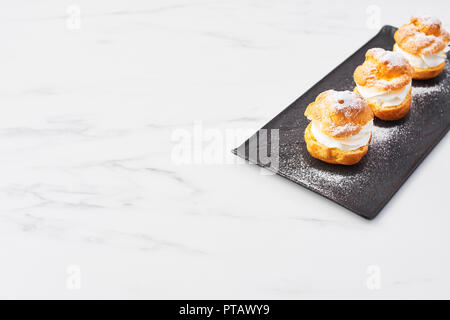 Vista dall'alto di deliziosa crema torte di sfoglia con panna e zucchero a velo su una piastra di nero su bianco tavola di marmo. Messa a fuoco selettiva, copia dello spazio. Foto Stock