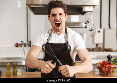 Iracondo chef cucinare in piazzale davanti alla cucina, tenendo siviera e frusta Foto Stock