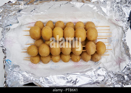 Intero fresco patate bambino nella loro camicie avvitato su spiedini di legno per grigliare accumulate su foglio di alluminio argentato concettuale del Barbecue, pic-nic, braa Foto Stock