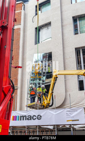 Impresa edile macis lavoratori su un cherry picker paranco con attenzione il montaggio di un nuovo grande finestra in vetro lastra in un edificio a Mayfair, London, Regno Unito Foto Stock