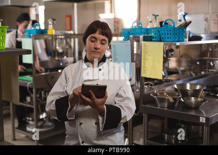 Lo chef femmina con tavoletta digitale in cucina Foto Stock