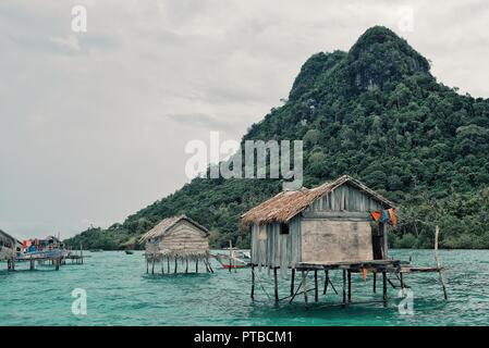 Stilt case in un mare bajau gypsy villaggio accanto ad una piccola isola sperone di roccia Foto Stock