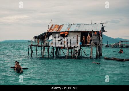 Stilt case in un mare bajau gypsy villaggio accanto ad una piccola isola sperone di roccia Foto Stock
