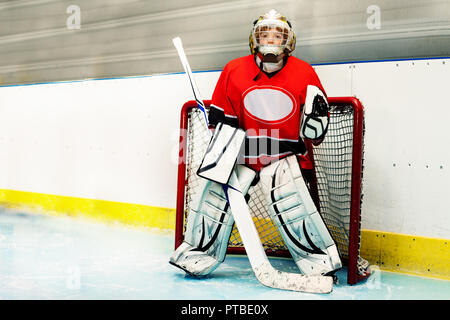 Ritratto di ragazzo adolescente, giovane goaltender in piedi con la mazza da hockey e di proteggere la rete Foto Stock