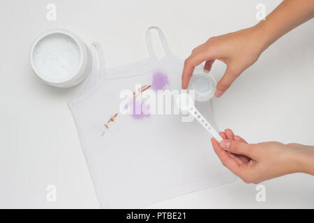 Ragazza mette su un bianco sporco T-shirt con macchie, rimuove le macchie e le mani, close-up, sfondo bianco, smacchiatore Foto Stock