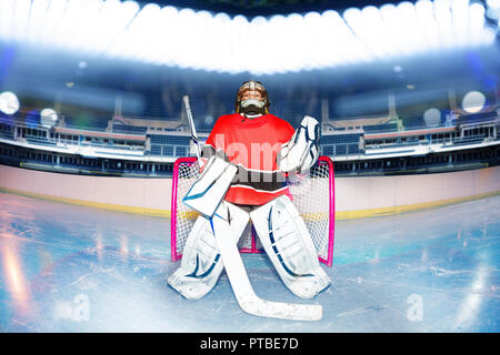 Ritratto di giovane goaltender in piedi accanto alla rete sotto le luci di ice hockey stadium Foto Stock