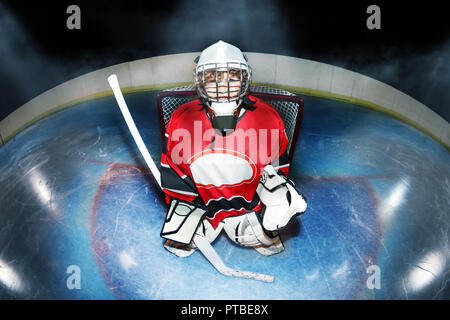 Vista superiore Ritratto di giovane goaltender, boy in attrezzature di protezione, in piedi con la mazza da hockey in l'obiettivo piega al ghiaccio Foto Stock