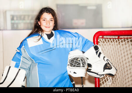 Ritratto di felice ragazza adolescente goaltender, in piedi accanto alla rete e tenere il casco in mano dopo la partita di hockey su ghiaccio Foto Stock