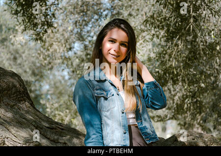 Bellissima con i capelli lunghi teen donna con capelli castani appoggiato su di un albero nel parco Foto Stock