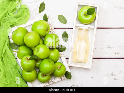 Bottiglia in vetro di fresco succo di mela biologico con mele verdi nella casella su uno sfondo di legno. Foto Stock