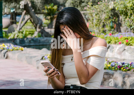 Preoccupato Hipster ragazza adolescente guardando il suo smart phone in un parco con un background non focalizzato Foto Stock