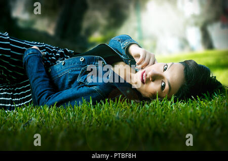 Carino giovane brunette reclino sull'erba nel parco godendo di un giorno di estate Foto Stock