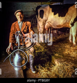 Brecon Beacons,Wales, Regno Unito, novembre 2,1988: un anziano contadino pone con la sua macchina di mungitura con mucche in procinto di essere munte in early morning sun. Foto Stock