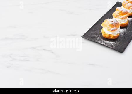 Vista dall'alto di deliziosa crema torte di sfoglia con panna e zucchero a velo su una piastra di nero su bianco tavola di marmo. Messa a fuoco selettiva, copia dello spazio. Foto Stock