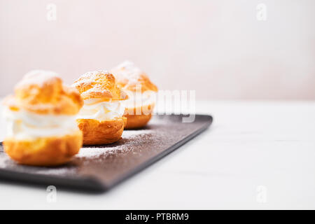 Deliziosa crema torte di sfoglia con panna e zucchero a velo su una piastra di nero su bianco tavola di marmo su sfondo rosa. Messa a fuoco selettiva, copia dello spazio. Foto Stock
