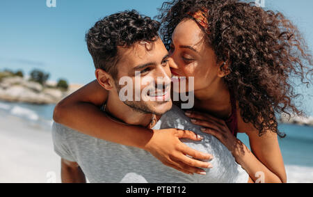 Donna sorridente piggy cavalcare il suo fidanzato e baciare lui. Uomo che porta la sua fidanzata sul suo retro all'esterno. Foto Stock