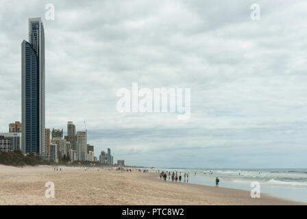 Vista lungo di Surfers Paradise beach con sabbia, mare, Anima Tower e nella distanza persone che passeggiano a bordo delle acque. Foto Stock