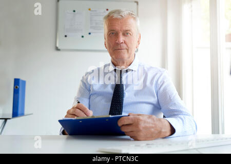 Ritratto di imprenditore senior seduto alla scrivania in ufficio e facendo alcuni documenti. Foto Stock