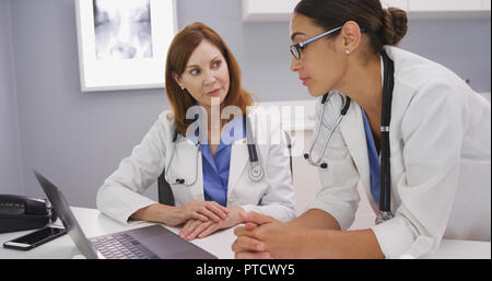 Giovane latina medico guardando al computer portatile e parlare con anziano medico Foto Stock