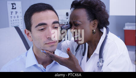 Ritratto di African senior medico utilizzando un otoscopio per ispezionare i giovani pazienti orecchio Foto Stock