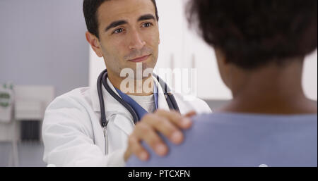 Bel maschio medico latino mettendo la mano sulla spalla di pazienti e consolante la sua Foto Stock
