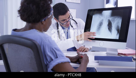 Senior nero donna ascolto di giovani latino MD come egli esamina la sua x-ray Foto Stock