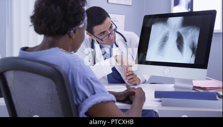 Senior nero donna ascolto di giovani latino MD come egli esamina la sua x-ray Foto Stock