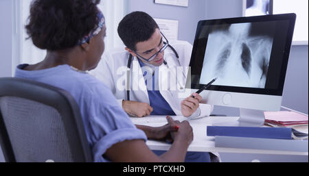 Senior nero donna ascolto di giovani latino MD come egli esamina la sua x-ray Foto Stock