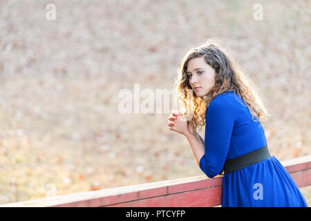 Giovane donna con mani giunte, pregando la preghiera, in piedi in natura in legno dipinto di rosso ponte sul torrente fiume durante il tramonto in autunno e inverno con Foto Stock