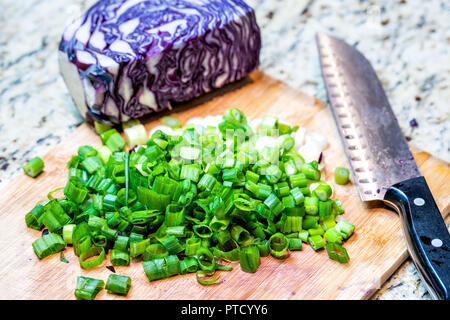 Tagliere, viola, cavolo rosso, di scalogni tagliati a fette, tagliare il cipollotto, coltello in cucina sul piano del banco in granito con nessuno durante la cottura e la preparazione di foo Foto Stock