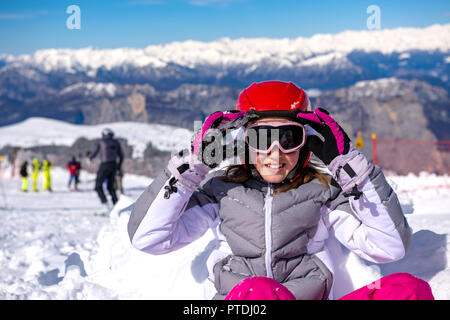 Piccola ragazza seduta nella neve indossando occhiali da sci Foto Stock