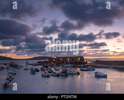 Lyme Regis, Dorset, Regno Unito. Il 9 ottobre 2018. Regno Unito Meteo: Moody mattina nuvole come sunrise colori illuminano il cielo sopra il Cobb, Lyme Regis. Credito: Celia McMahon/Alamy Live News Foto Stock