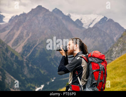 L'uomo fotografo con grande zaino e tenendo la fotocamera foto di montagna. Stile di vita viaggio avventura concetto vacanze attive outdoor Foto Stock
