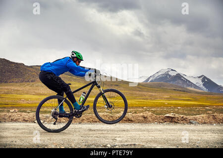 Uomo in mountain bike sulla strada in alta montagna contro il cielo nuvoloso sfondo. Foto Stock