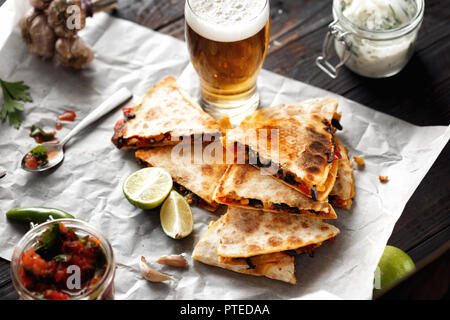 Birra vegetariano snack: quesadilla con verdure e formaggio in legno scuro con piano in vetro di birra lager Foto Stock