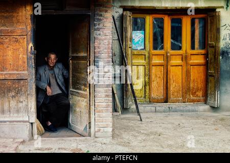 Monastero di Labrang, Xiahe, provincia di Gansu / Cina - 6 GIU 2011: locale abitante seduto alla sua casa porta a guardare la folla per passare da Foto Stock