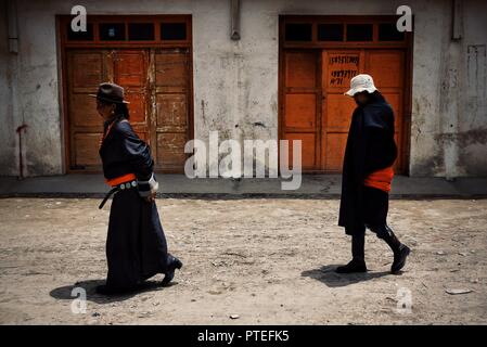 Monastero di Labrang, Xiahe, provincia di Gansu / Cina - 6 GIU 2011: buddista tibetana pellegrino donna e uomo a camminare di fronte red porte in legno traditio Foto Stock